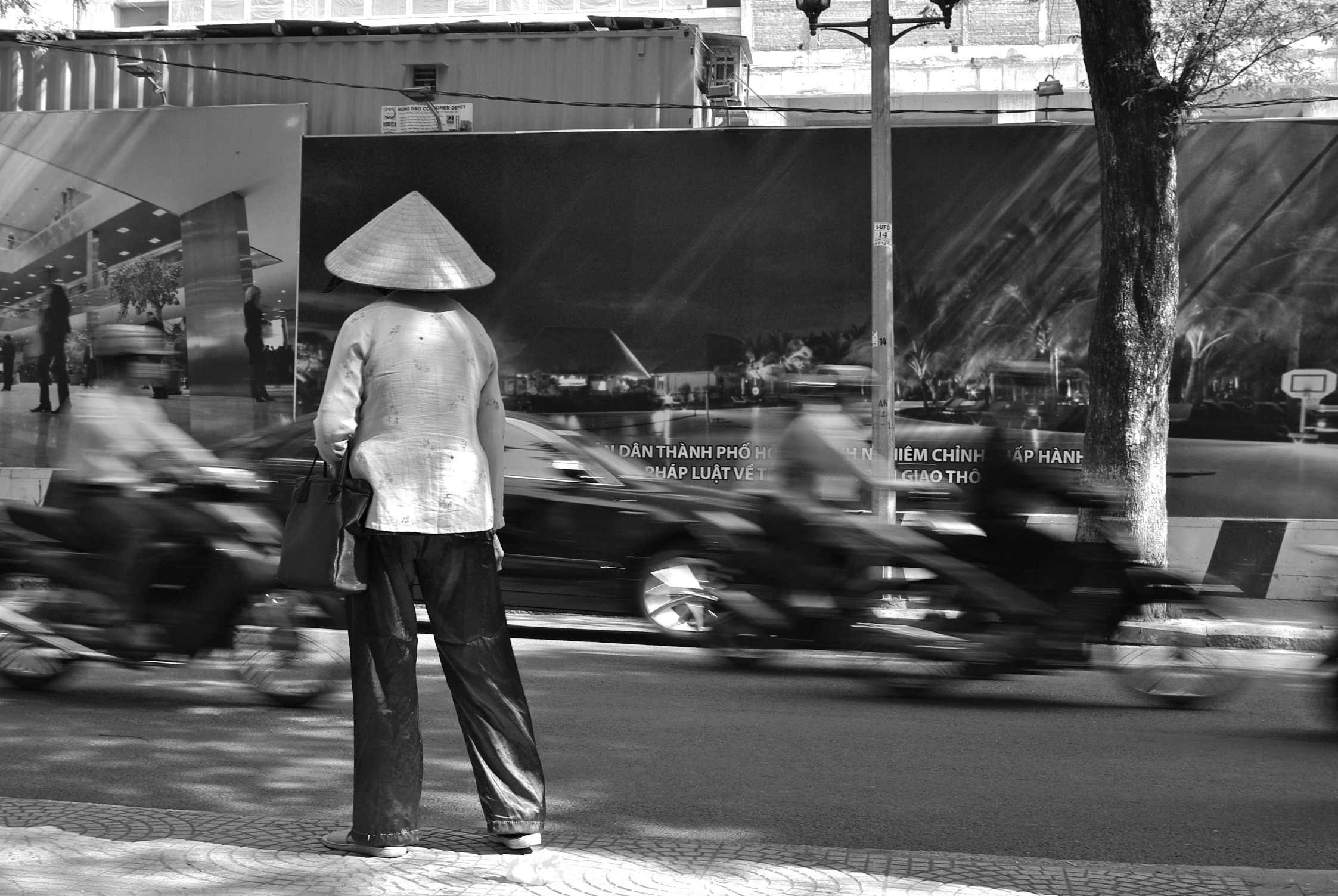 Ho Chi Minh Ville, mutations rapides, rêves de modernité, circulation dense. Sur le bord du trottoir, une femme hésite. Elle semble venir d’ailleurs, d’un monde ralenti, des campagnes vietnamiennes. Cliché : Pascal Clerc